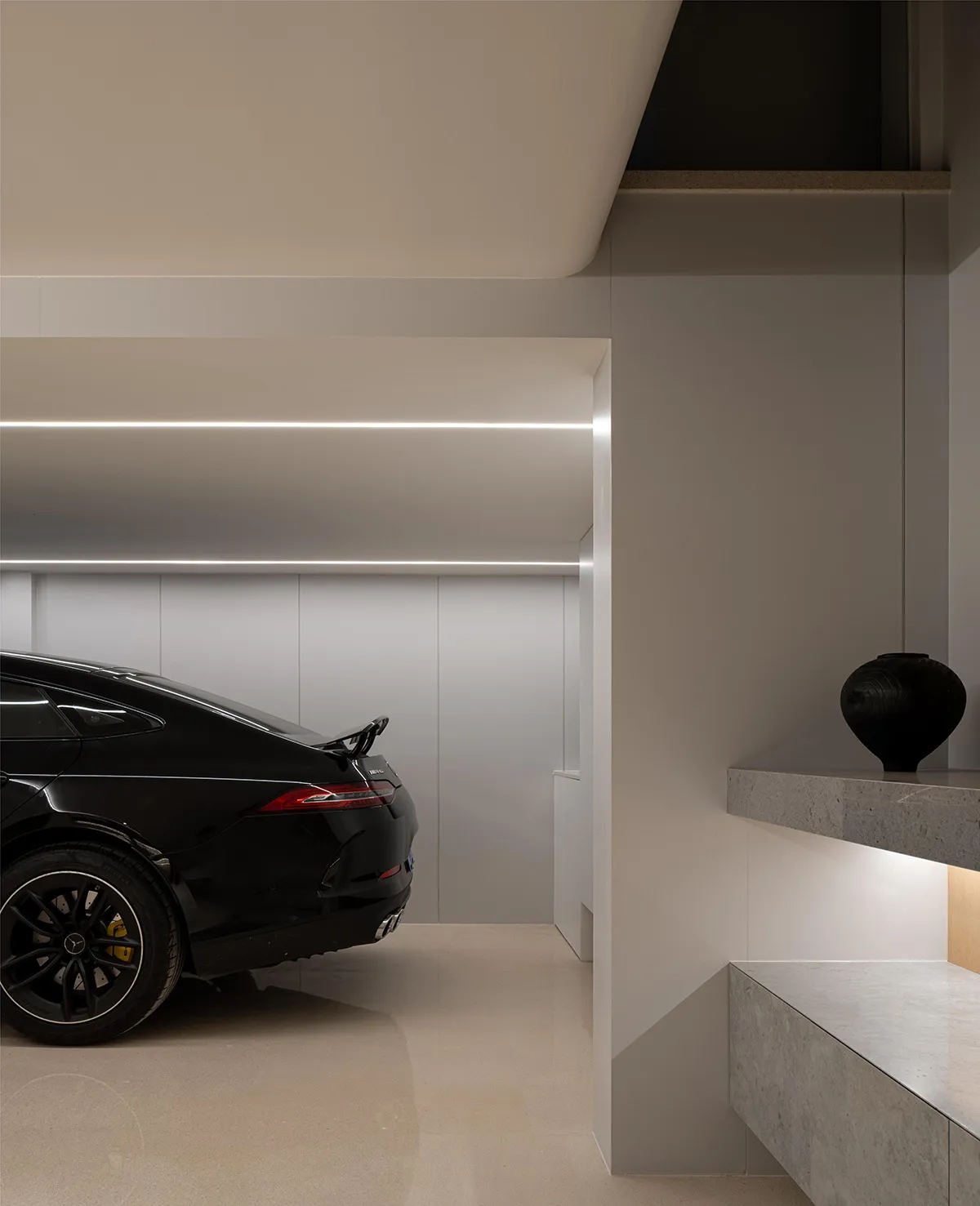 Modern garage interior with a sleek black car, concrete flooring, and minimalist design.
