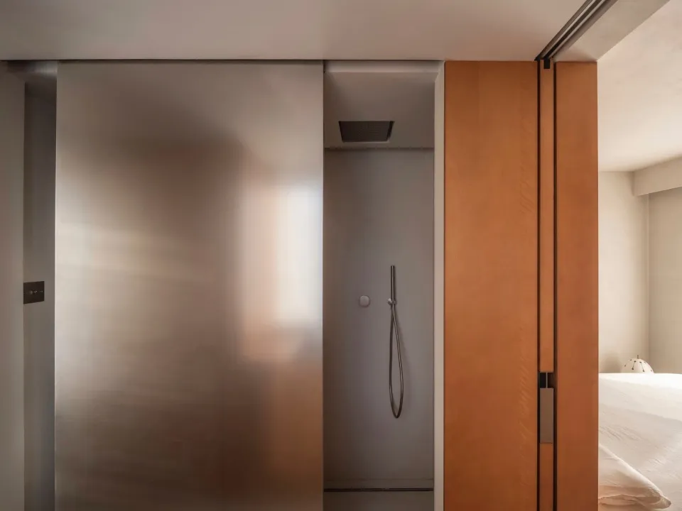 A modern minimalist bathroom with a frosted glass sliding door and a metal shower head.