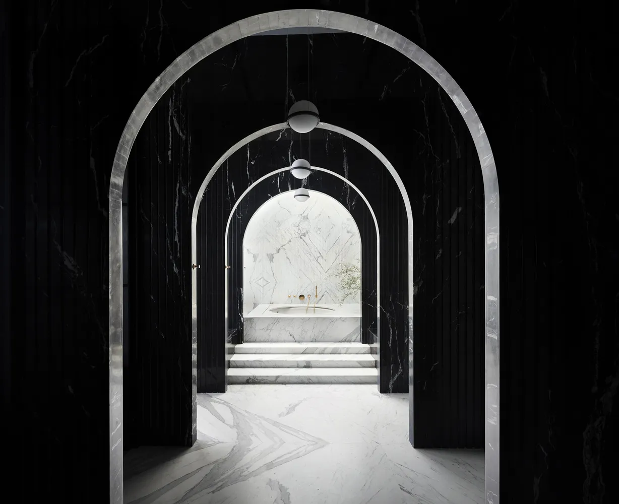 A modern minimalist bathroom with black marble walls and a white marble bathtub surrounded by recessed archways.