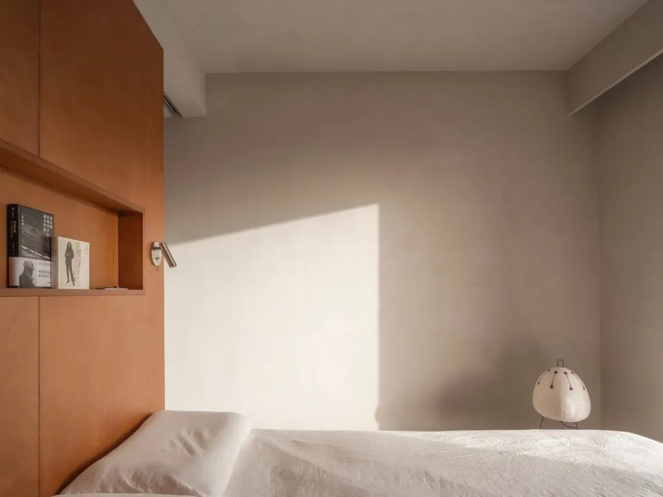 Minimalist bedroom featuring a white sheet-covered bed with a wooden headboard and a white floor lamp.