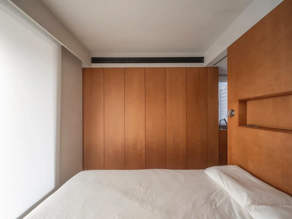 A minimalist bedroom with a white bed and wooden paneled walls.