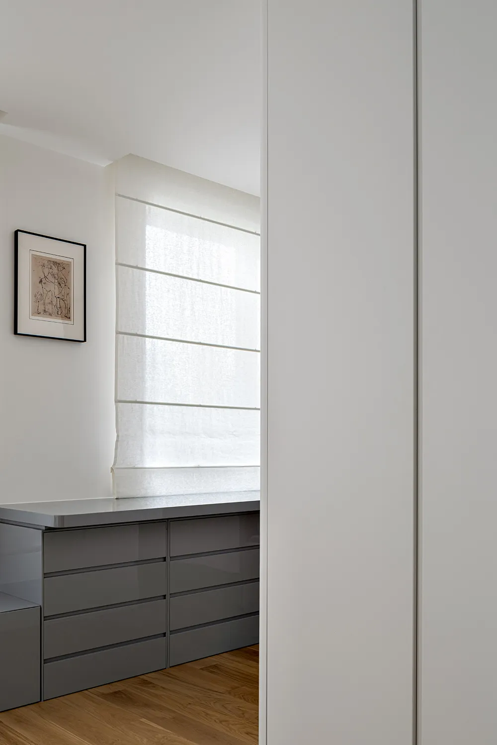 Modern gray kitchen cabinets situated by a window sill with sheer white curtains.