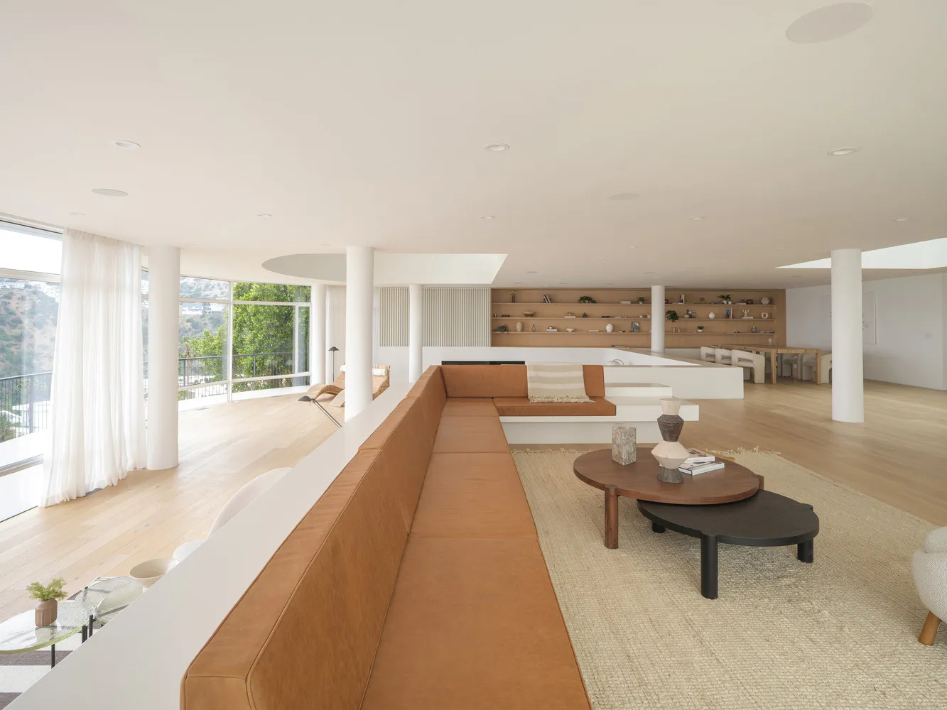 Modern living room featuring a long brown leather sofa, wooden flooring, and white walls.