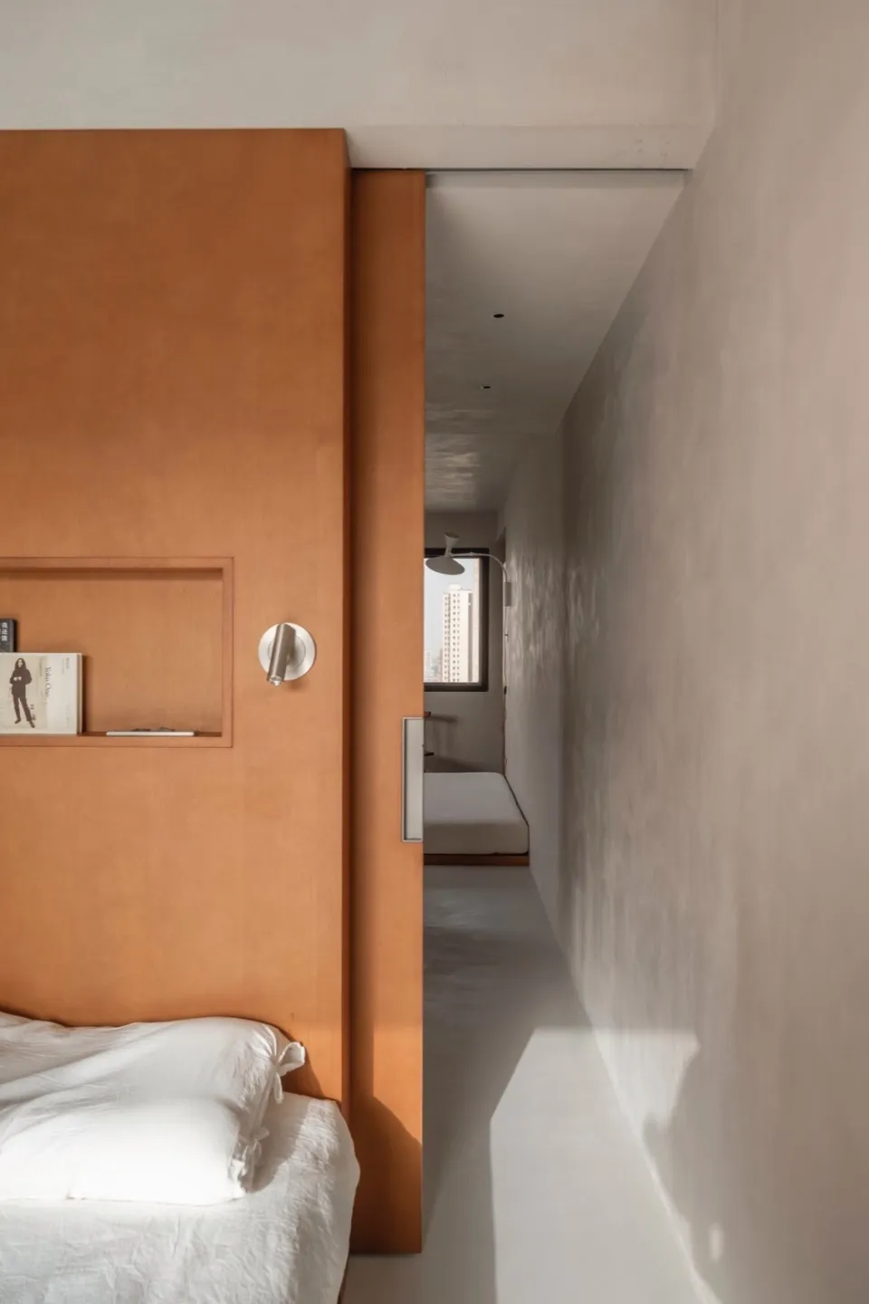 Minimalist bedroom featuring an orange wood headboard with a white bedspread