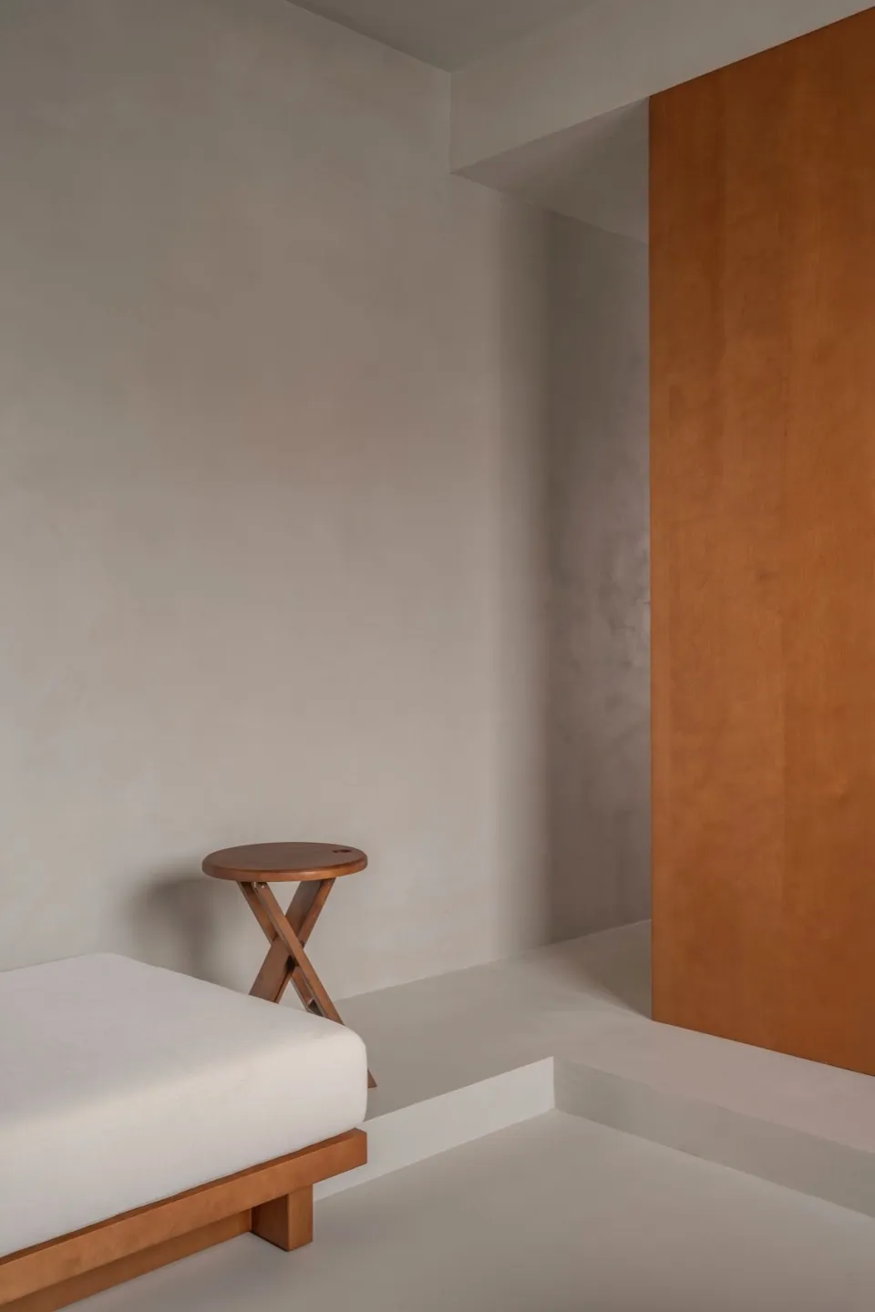 A minimalist bedroom featuring a wooden bed and concrete walls, creating a serene and modern atmosphere.