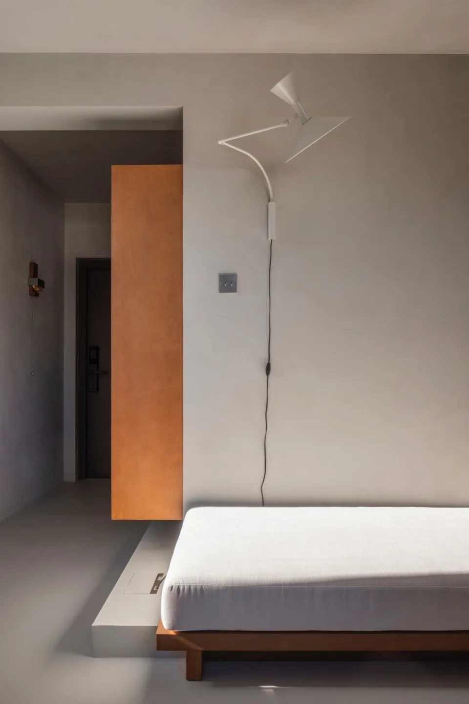 Minimalist bedroom featuring a concrete bed platform, wall-mounted lamp, and wooden accents.