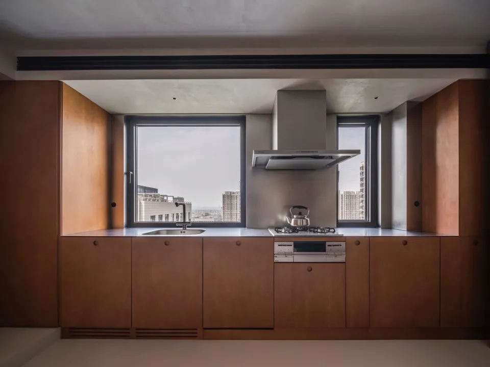 A modern minimalist kitchen with wooden cabinetry and a large window overlooking urban skyline.