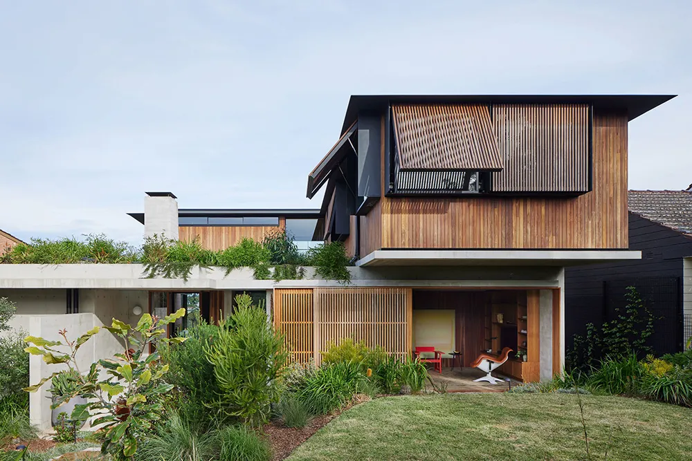 A modern house featuring a combination of concrete and wood exteriors, with a greenery rooftop and a partially open wooden ga