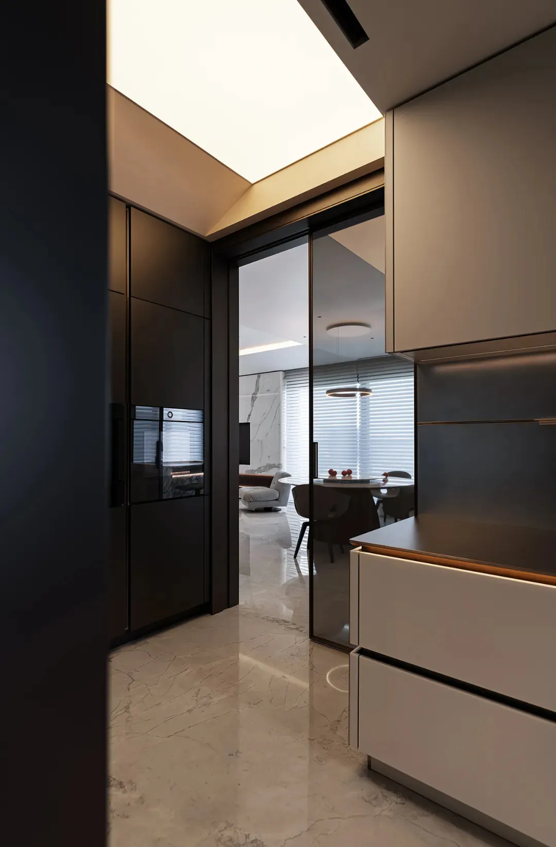 Modern kitchen and dining area with marble flooring and sleek, white cabinets.