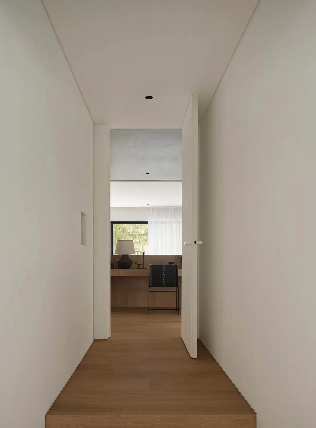 A minimalist hallway with wooden flooring and white walls, featuring a door leading to another room.
