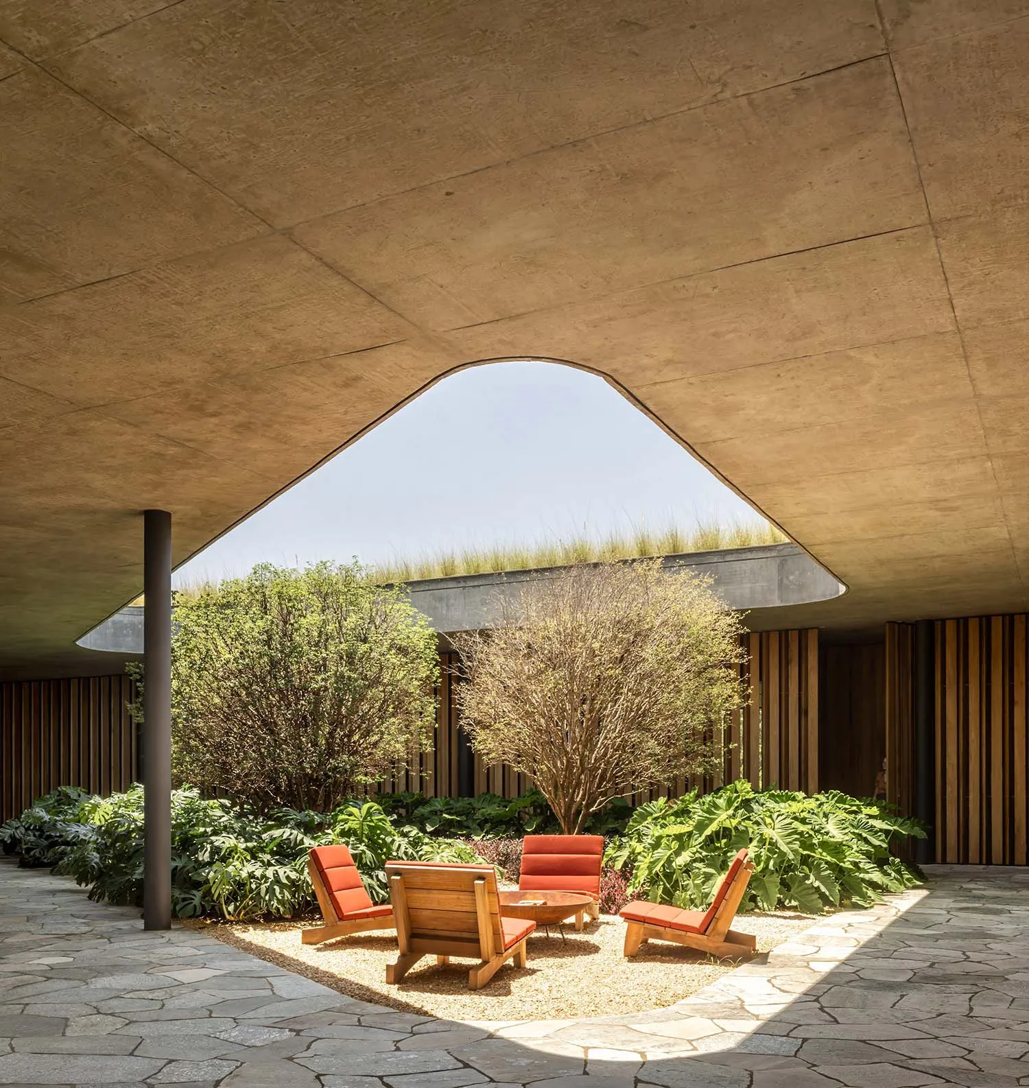 現代室內休憩區，木椅置於礫石地面，周圍環繞綠意，搭配拱形屋頂與自然氛圍