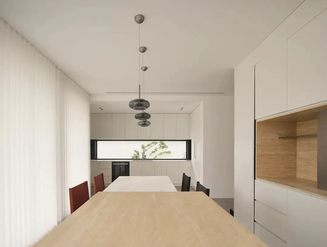 A modern minimalist kitchen space with white materials, black countertops, and wooden accents.