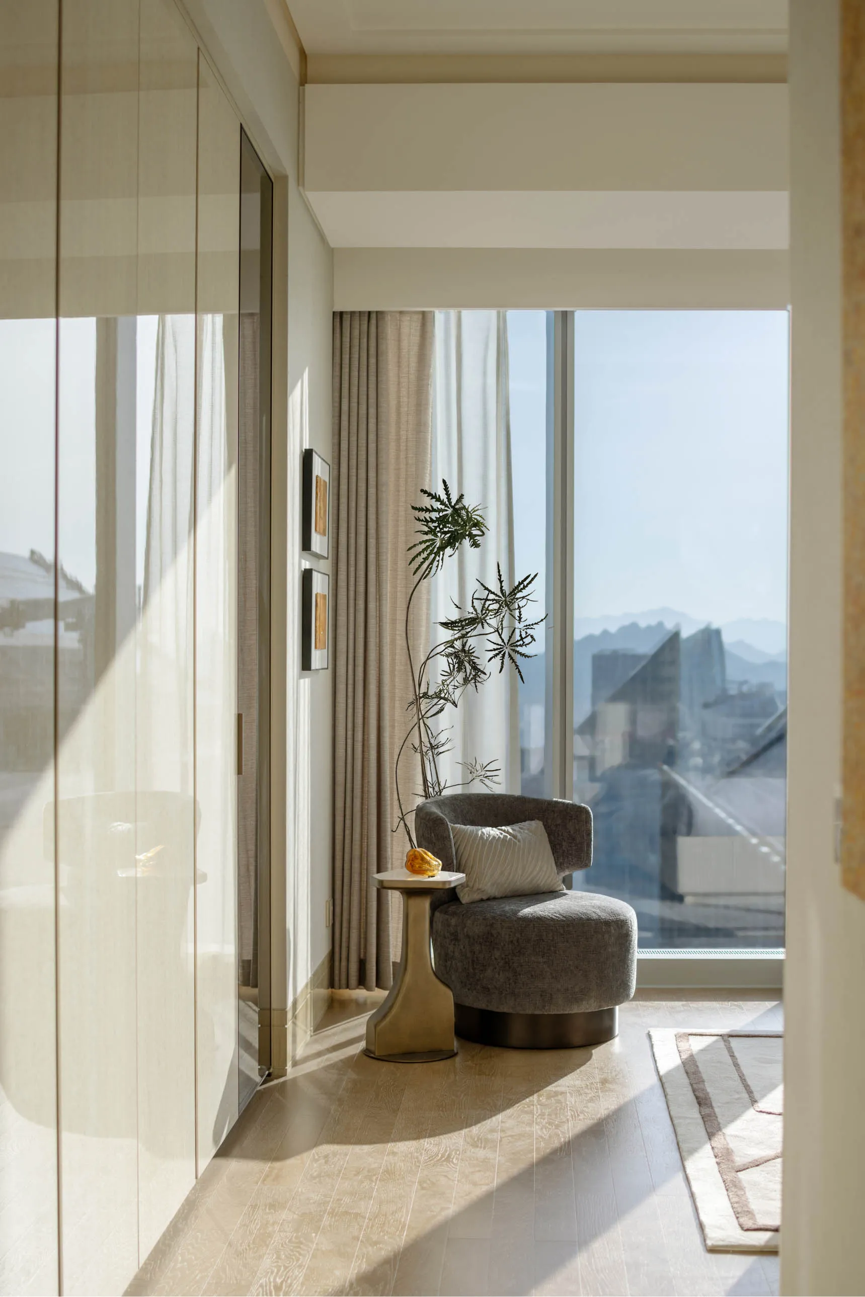 A modern residential interior featuring a comfortable living area with fabric seating, glass window, and metal accents.