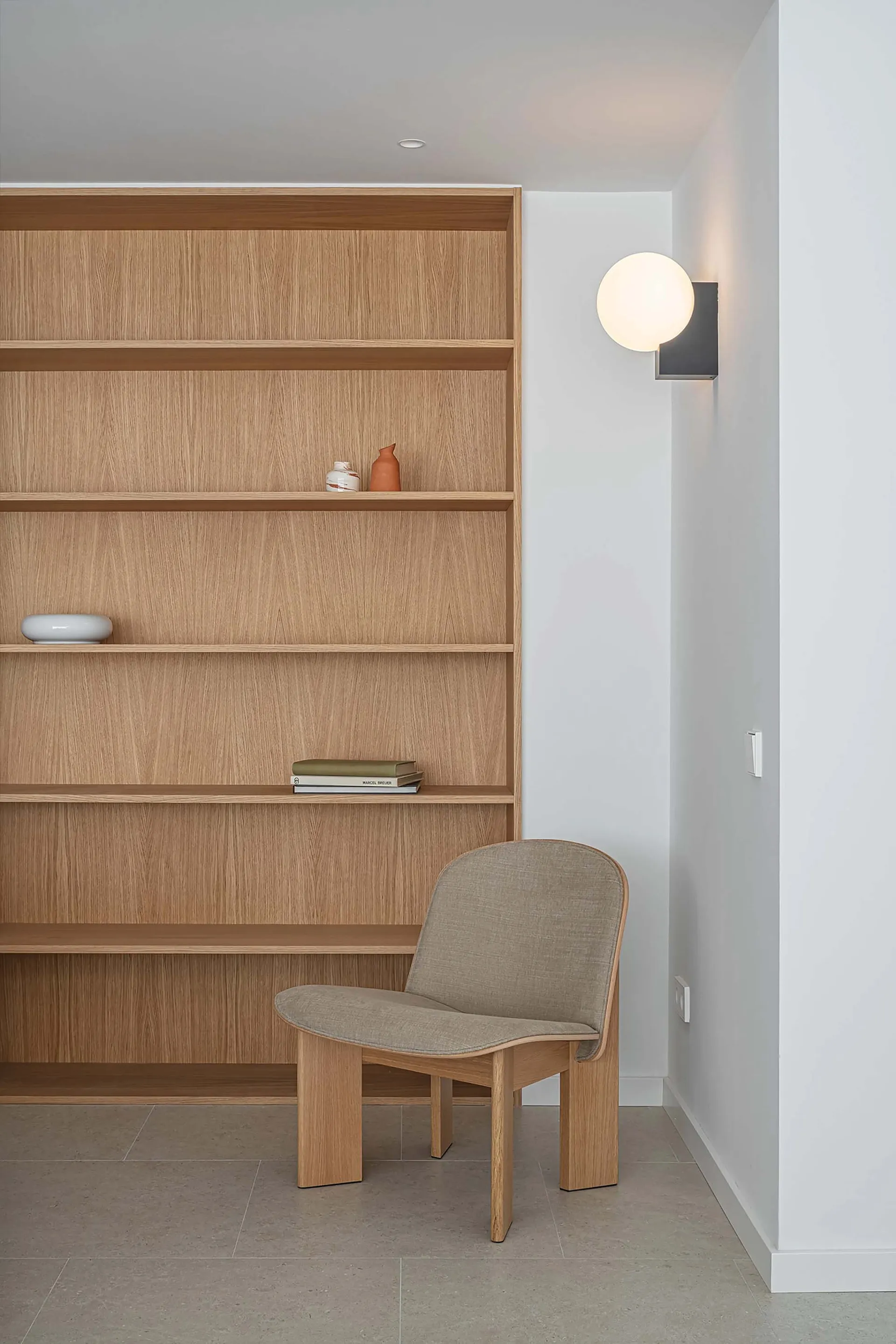 Minimalist reading corner featuring wooden shelves with a few books and decorative items.