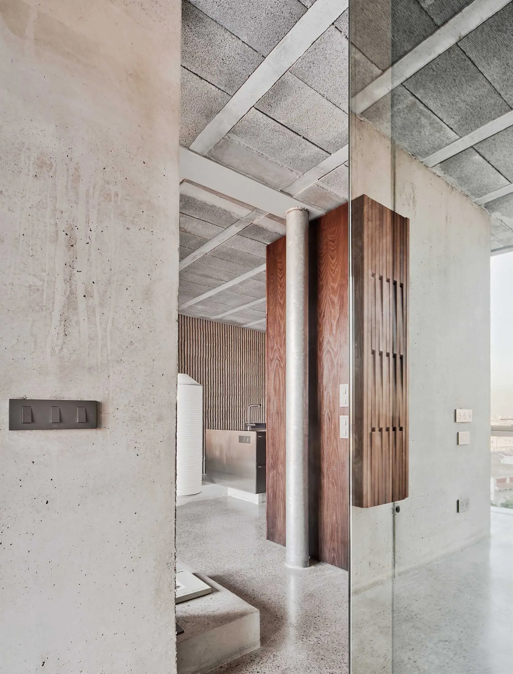 A modern living room with concrete walls, wooden accents, and open space.