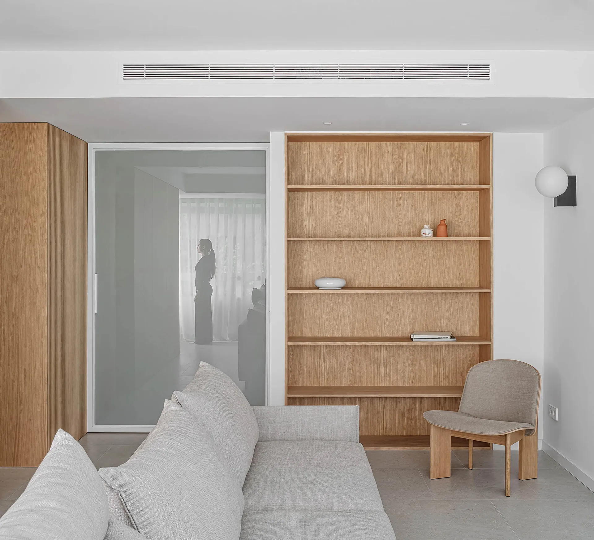 A modern living room featuring light-colored wood shelves and furniture, with a person standing in the background.
