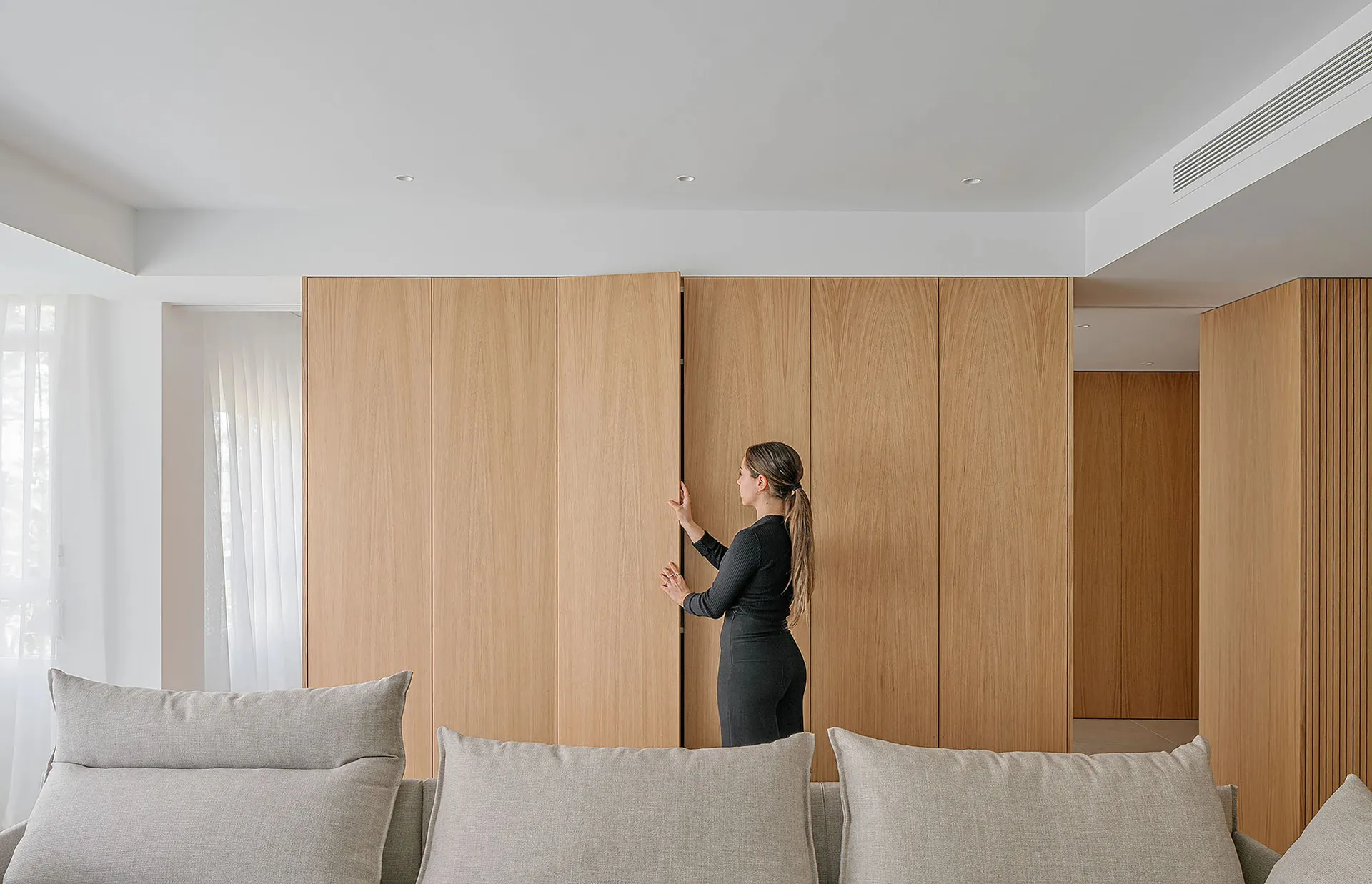 A woman in a modern living room with wooden walls and a light gray sofa.