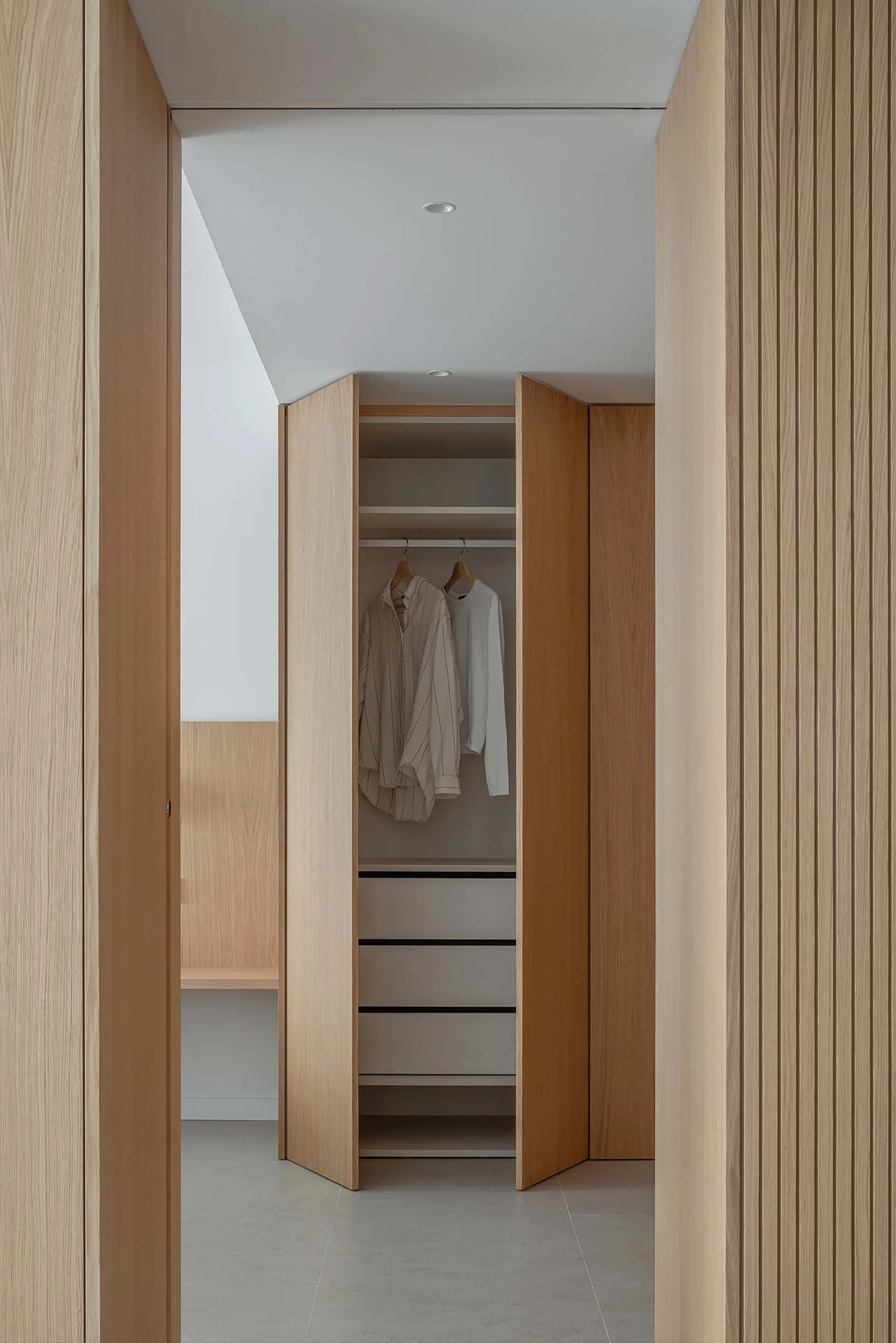 Modern-style walk-in closet with wooden hanging rails and minimalist design, featuring a white ceiling and grey floor tiles.