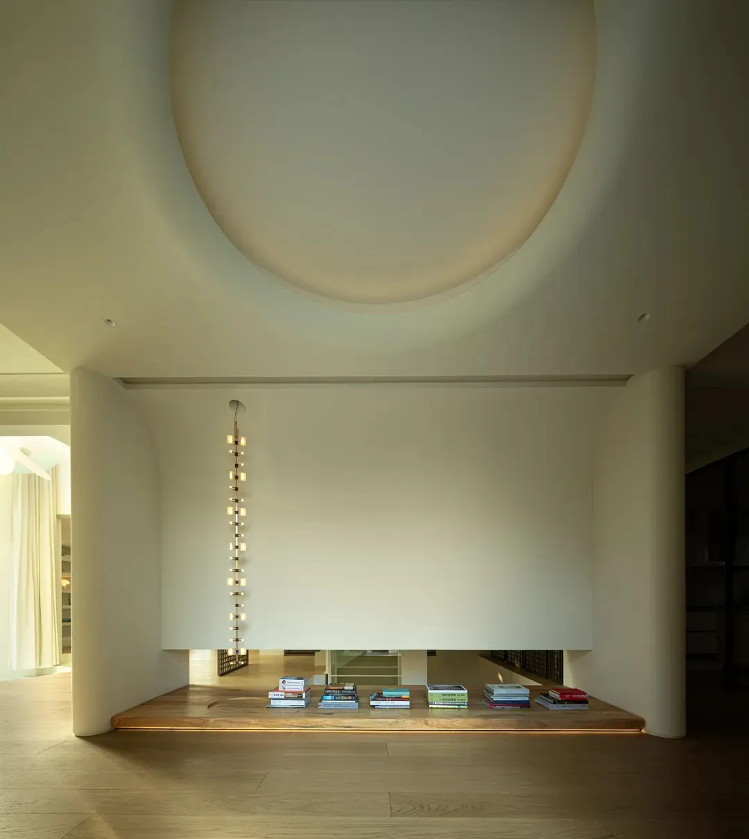 A minimalist living room with a wooden floor and a modern light fixture.