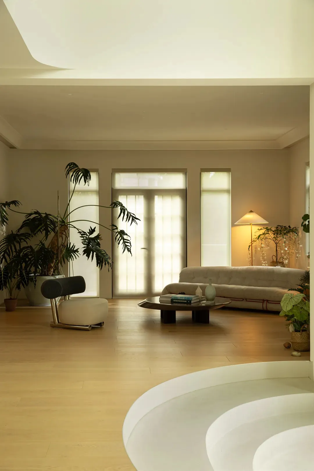 A minimalist living room with wooden flooring, a beige sofa, and a round table with books and vases.