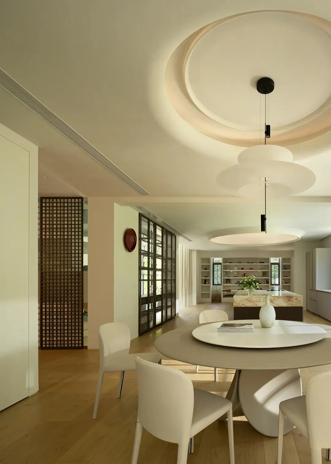 A modern dining room featuring metal and plastic materials with a round table and chairs, a central pendant light, and a book