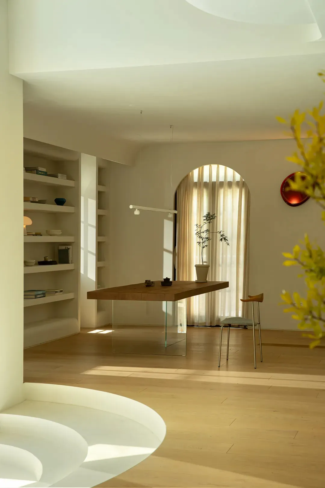 Modern home office featuring a glass and wood table with a plant and a stool.