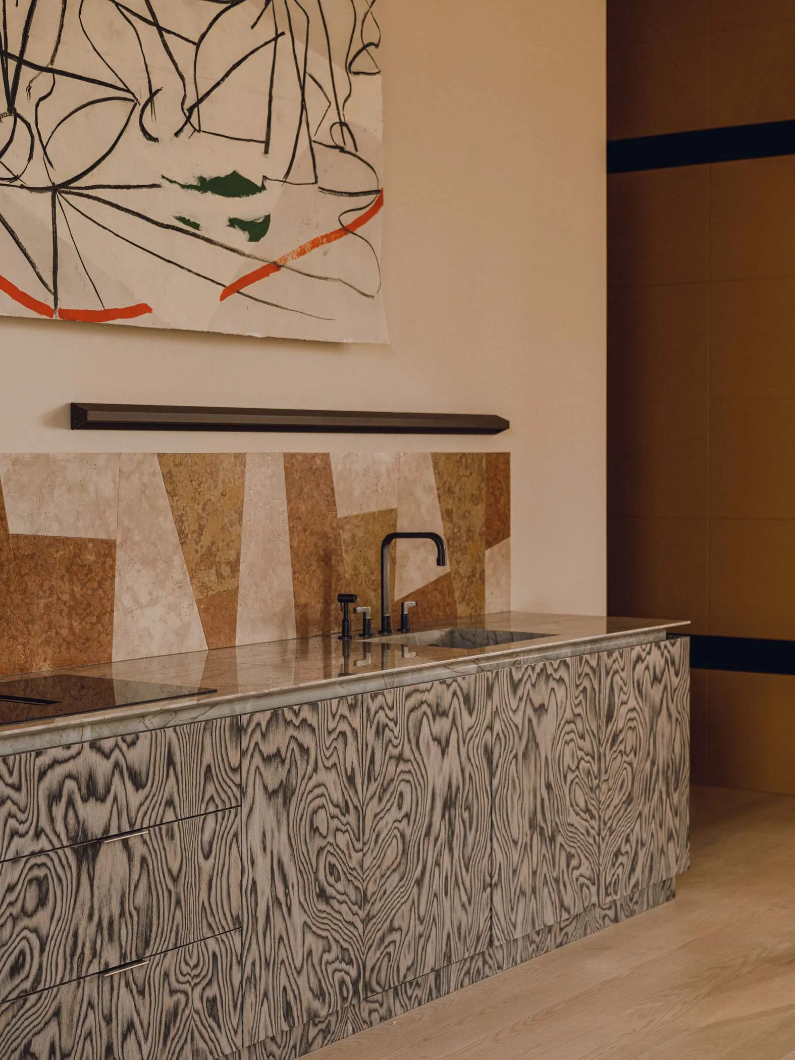 A modern interior space featuring a wooden counter with a sink and faucet, surrounded by abstract artwork and a mix of neutra