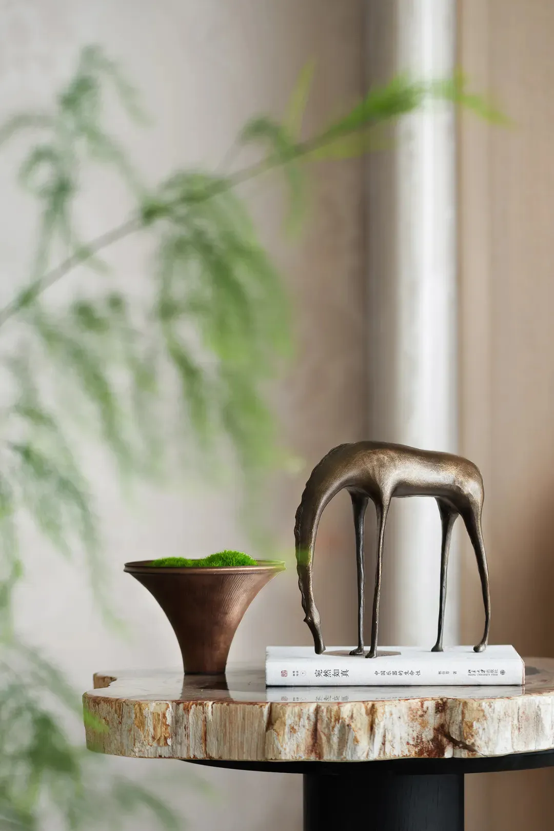 A modern metal deer sculpture placed on top of a bookshelf with a book.