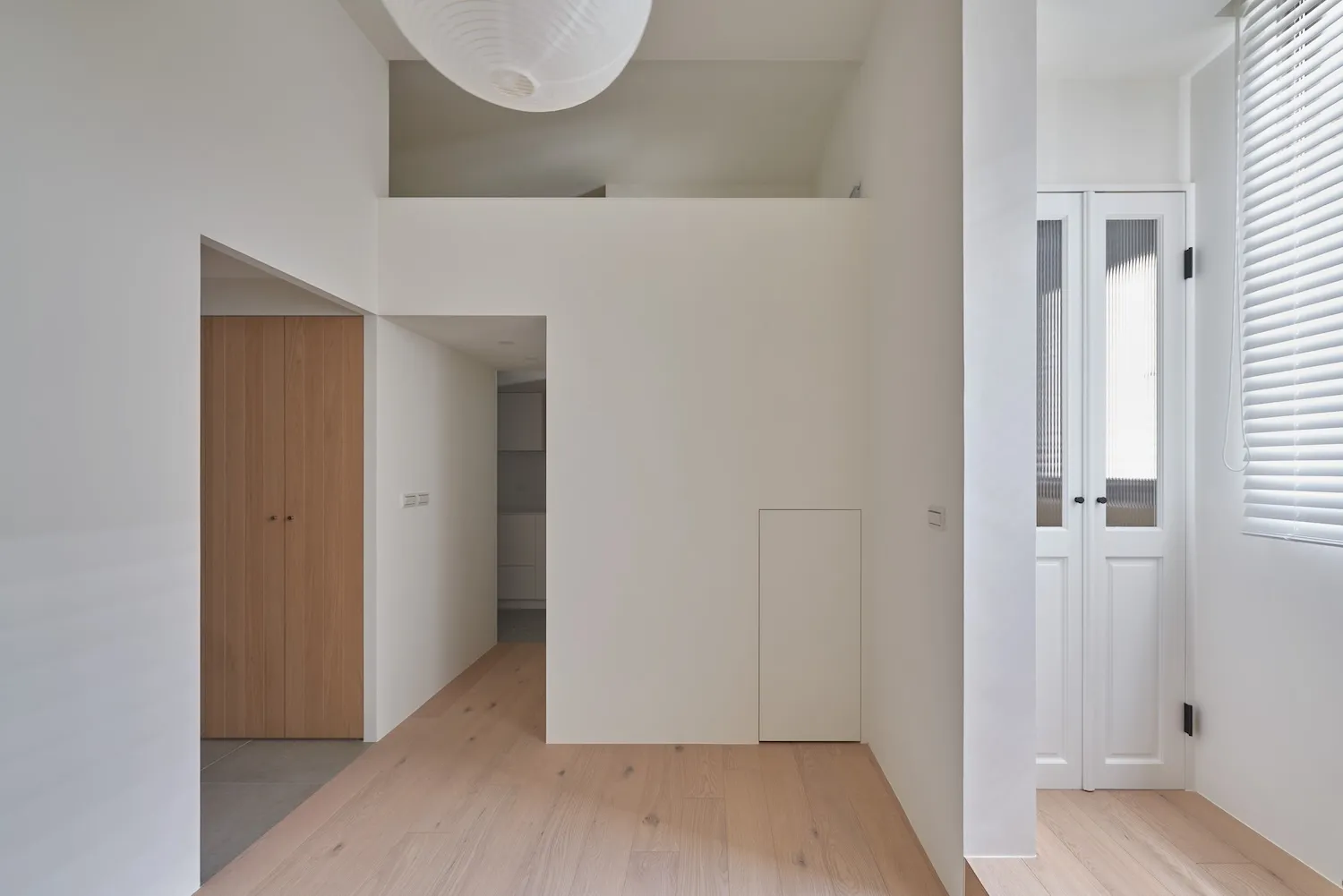 Modern minimalist residential hallway with white walls, wood flooring, and a white overhead light fixture.