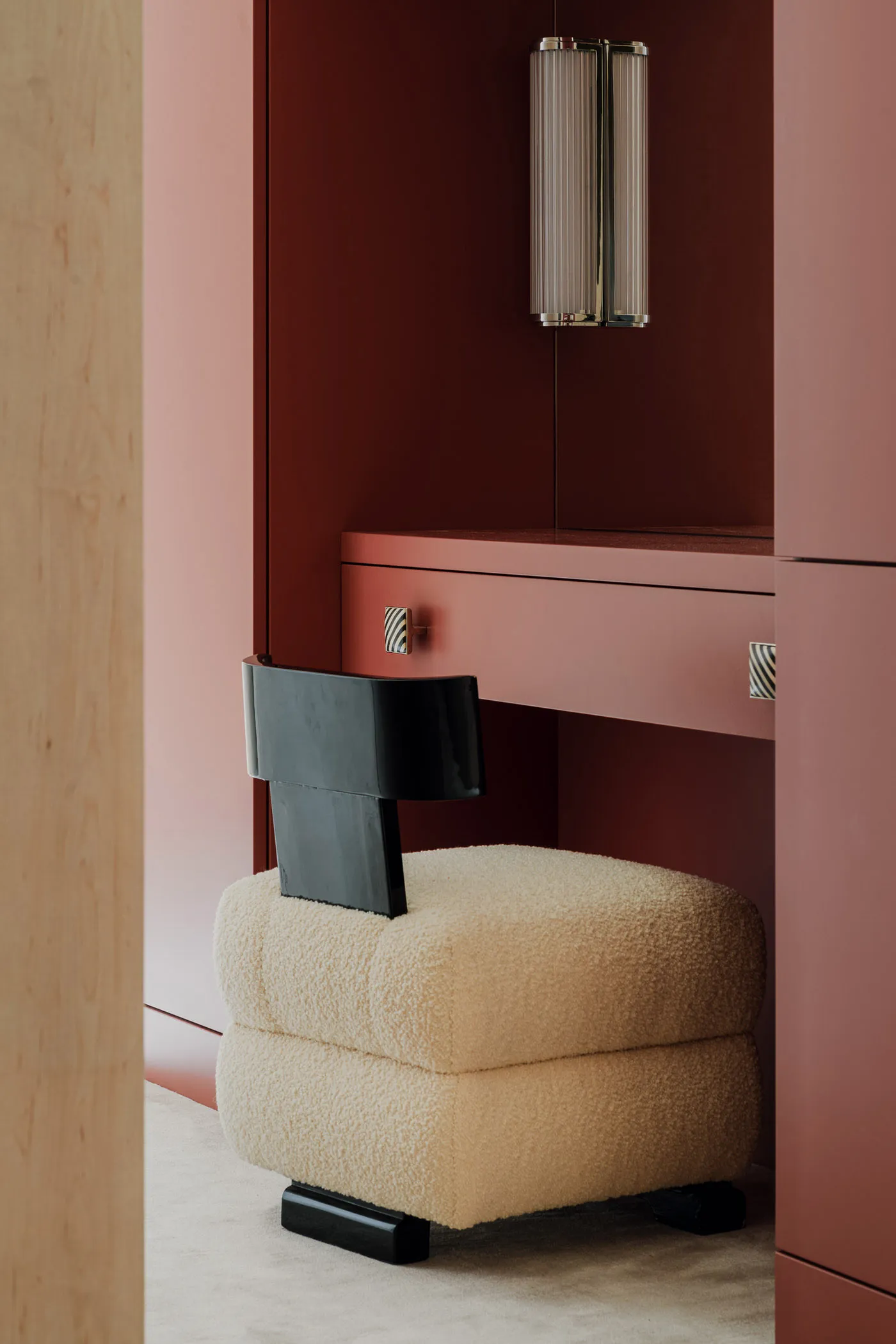 A modern vanity desk with a white fabric base and a black chair, featuring a wall-mounted light fixture.