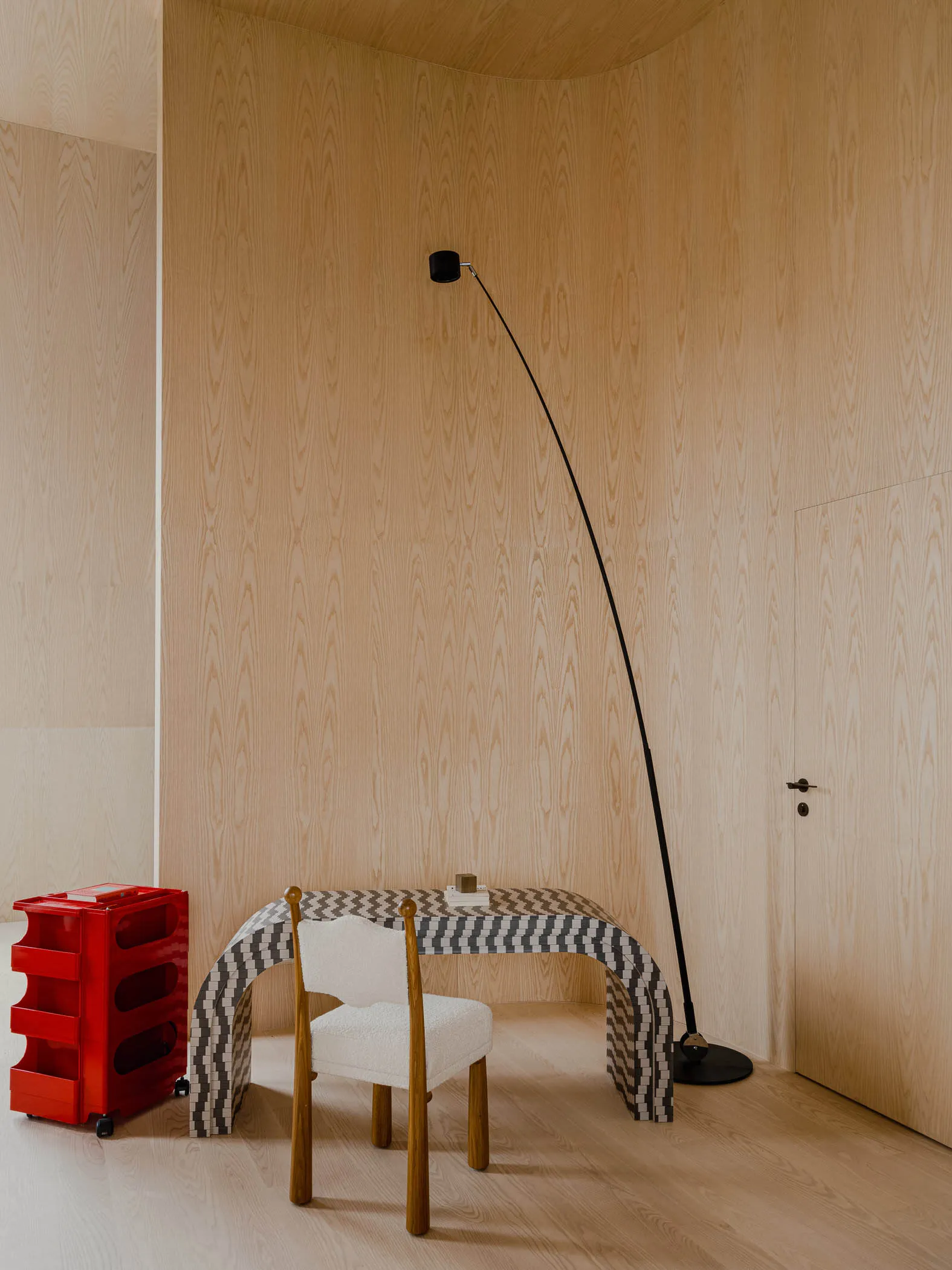 A modern workstation with a unique curved desk, a white upholstered chair, and a red rolling cart with transparent drawers in