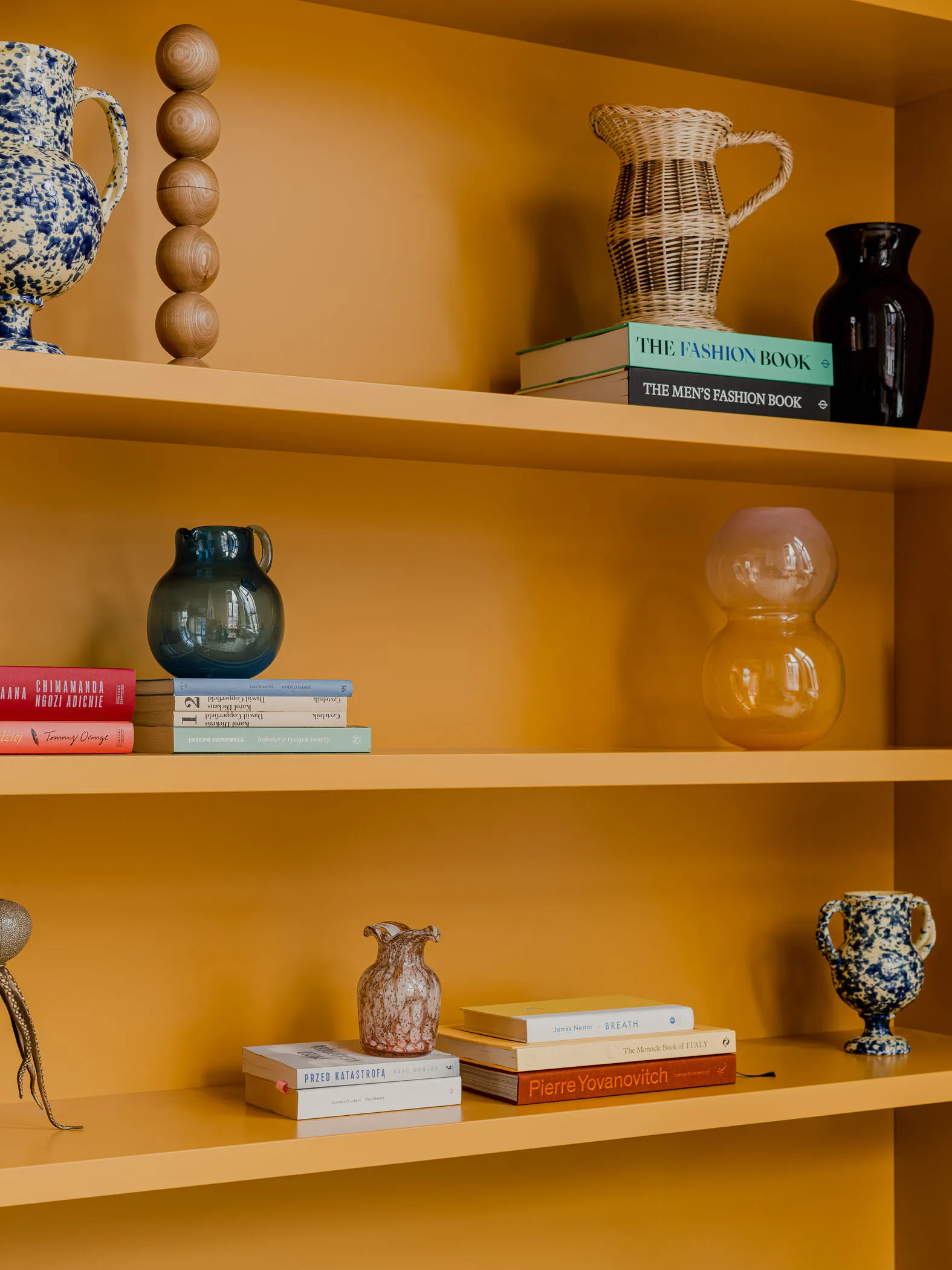 Three shelves adorned with colorful ceramics, glassware, and books.
