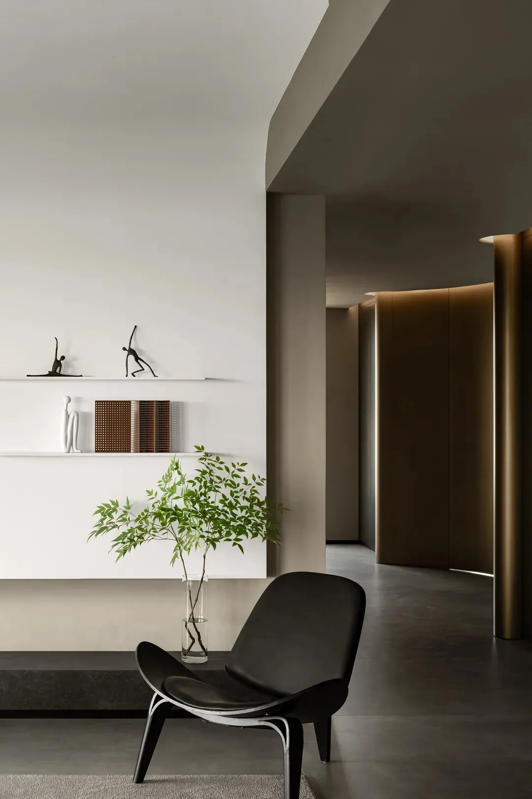 Minimalist living room with concrete floor and wall, featuring a black leather armchair, a plant in a vase, and a shelf with