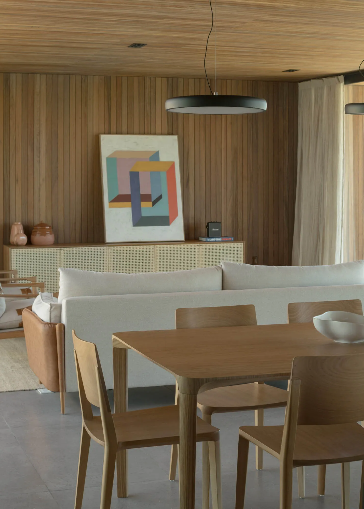 A minimalist living room with a wooden dining table, chairs, and sofa, complemented by a wooden floor and ceiling. Geometric