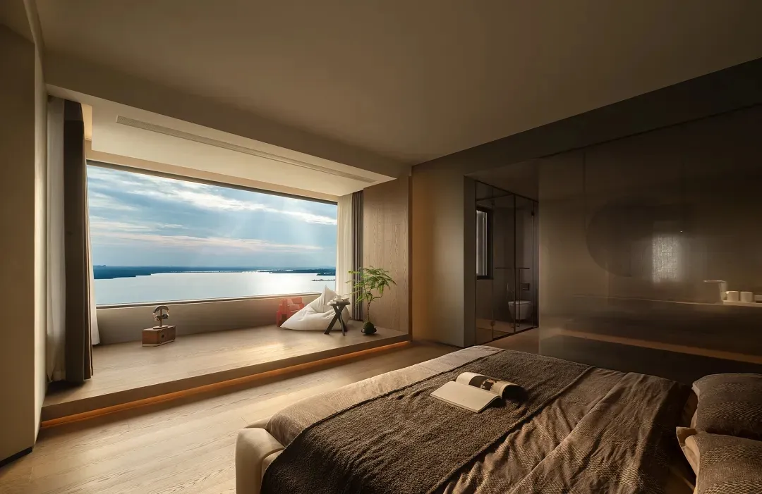 A modern bedroom with a large window overlooking a lake, wooden flooring, and a cozy seating area.