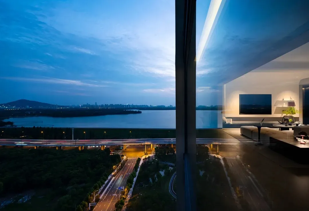 A modern living room with a glass window overlooking a cityscape at dusk.