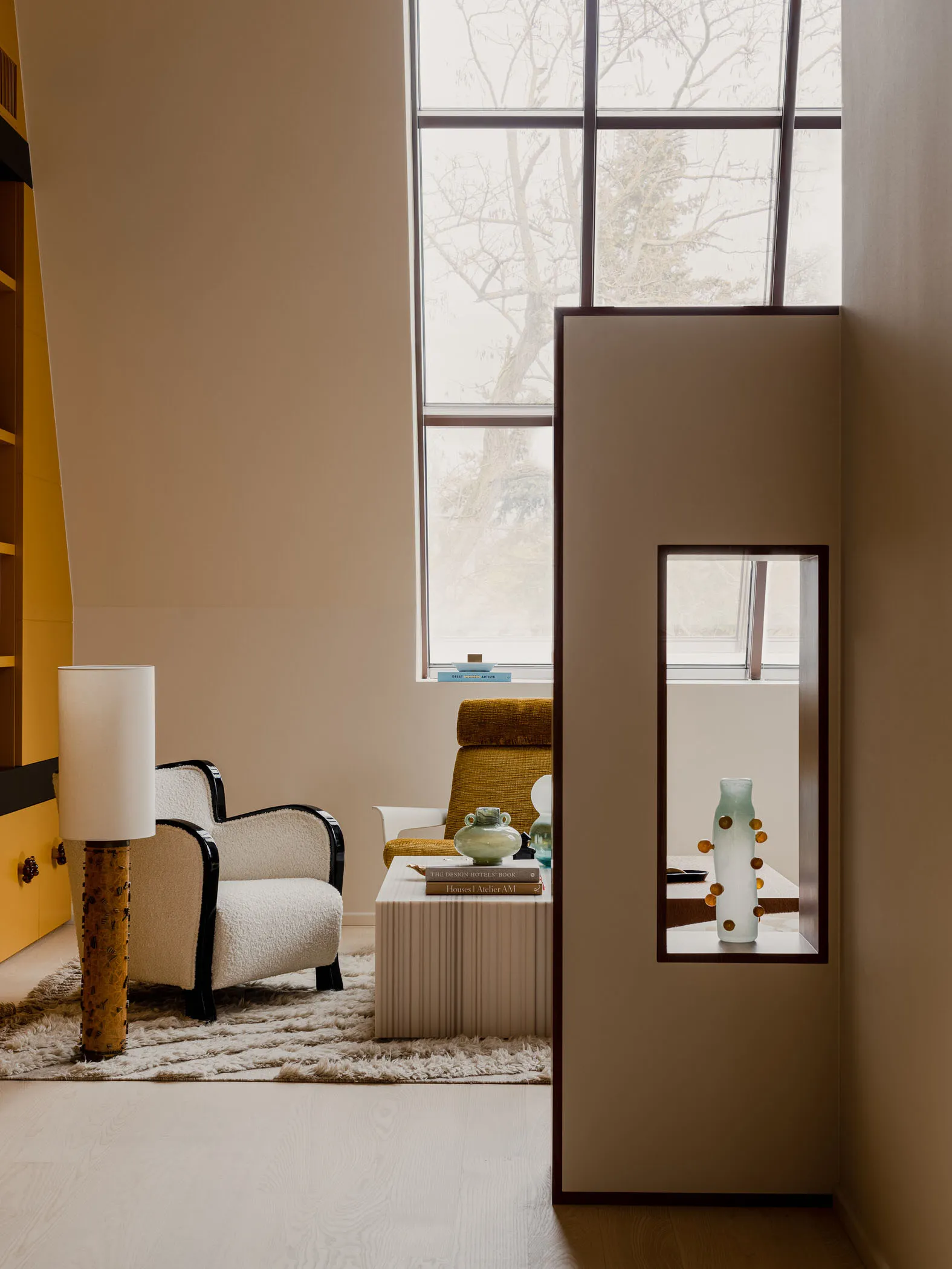 Modern living room with minimalist design, featuring a white armchair, a yellow sofa, and a tall glass vase on a side table.