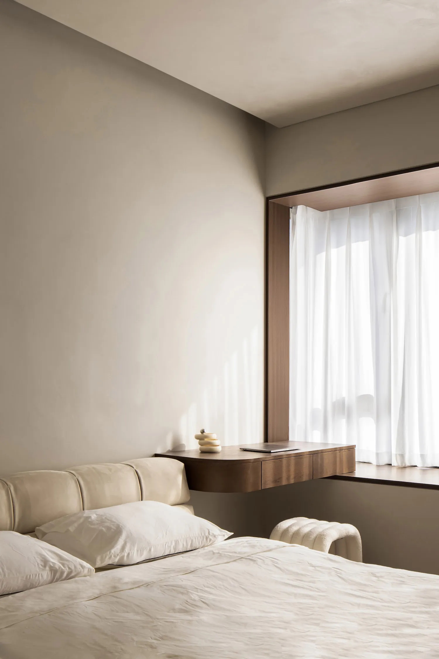Minimalist bedroom featuring a bed with white linens and a wooden floating desk by the window.