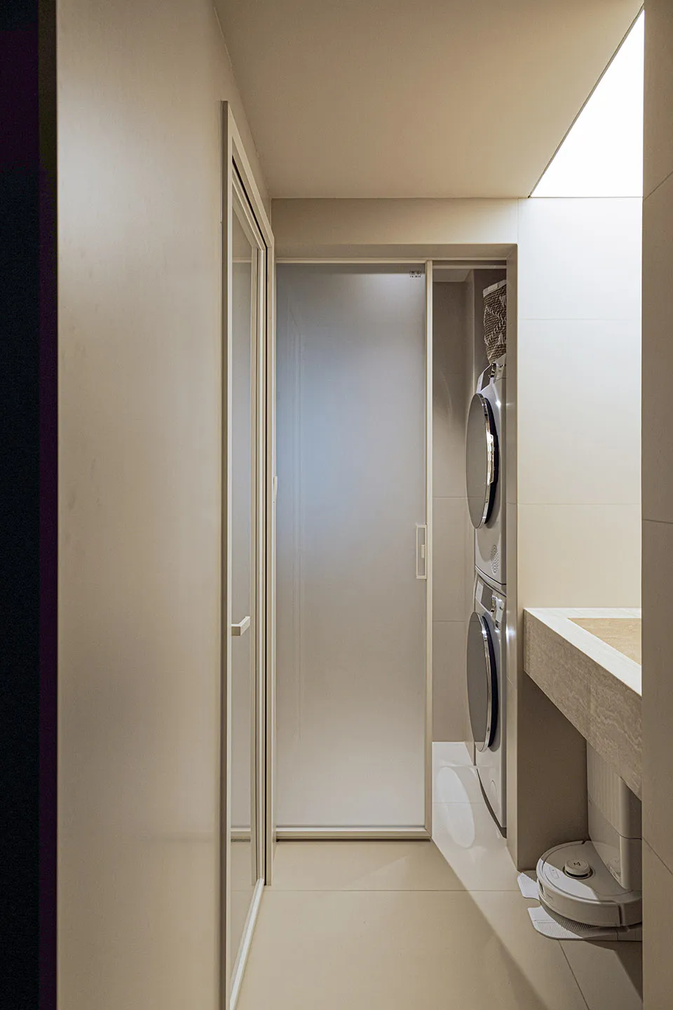 A minimalist modern bathroom and laundry room with tiled walls, featuring a clear shower door and washing machines.