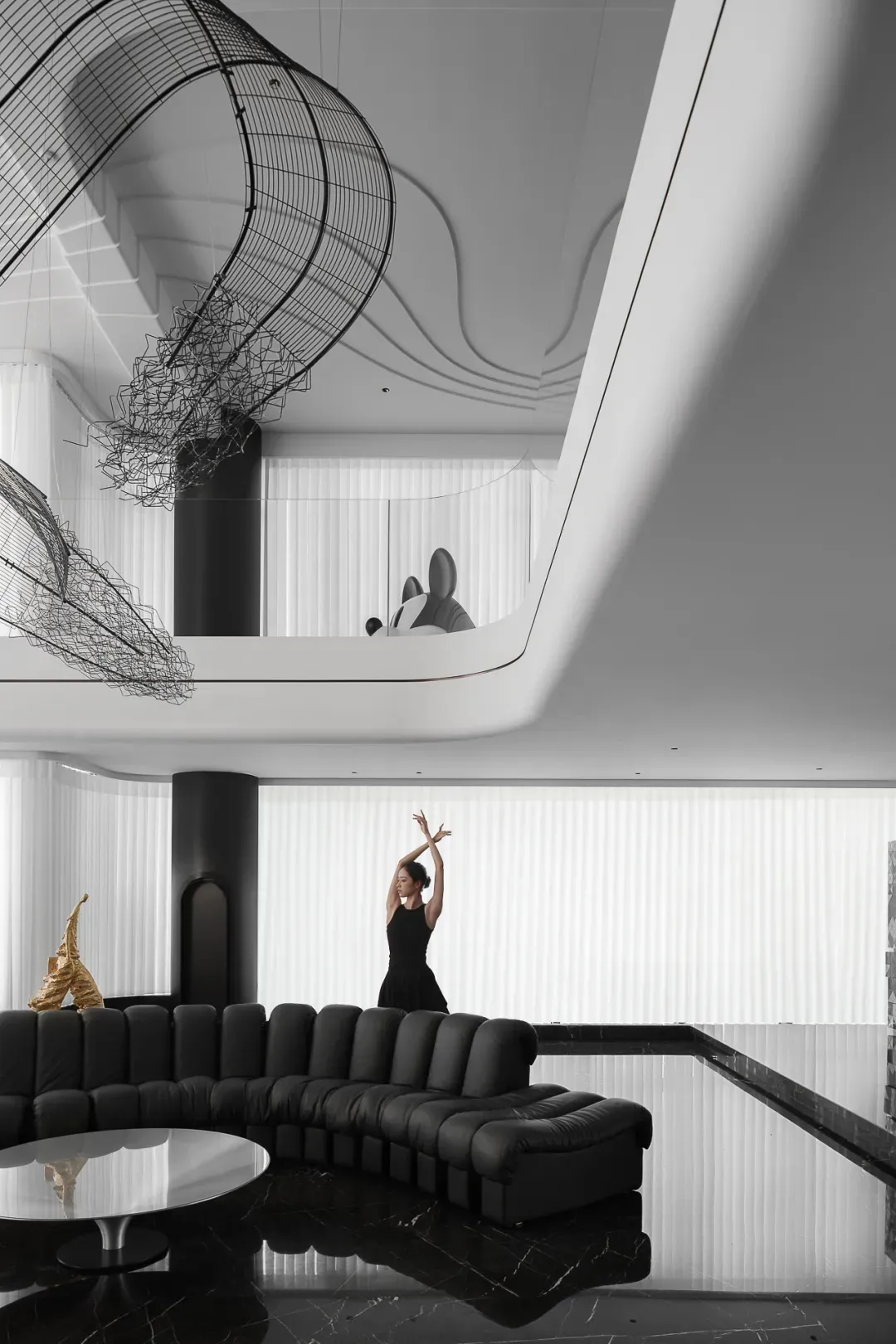 A modern black and white lobby interior featuring a suspended metal sculpture, a sleek black sofa, and a large window with ve