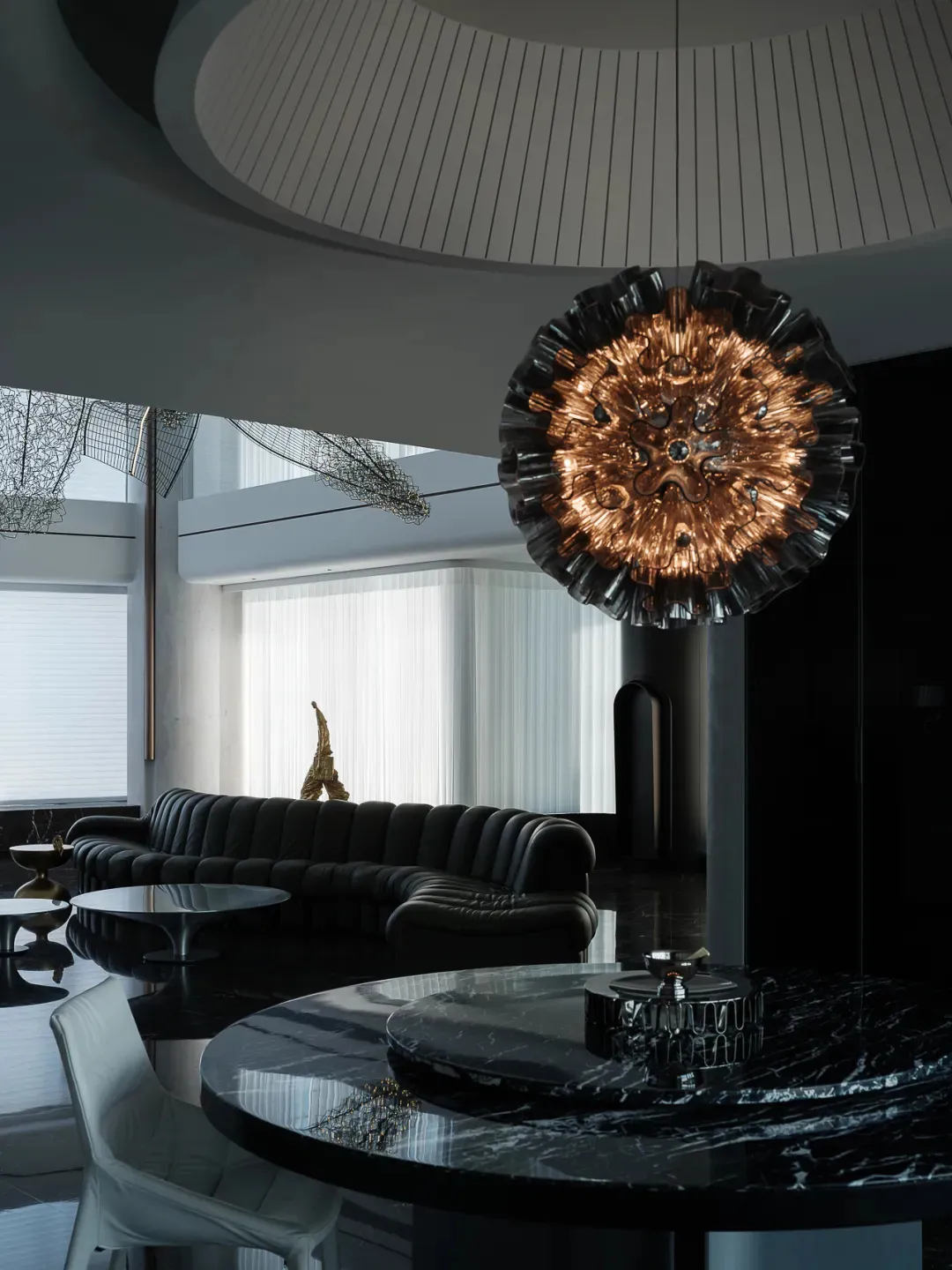 A modern living room featuring a black leather sofa, a round marble table, and a unique chandelier.