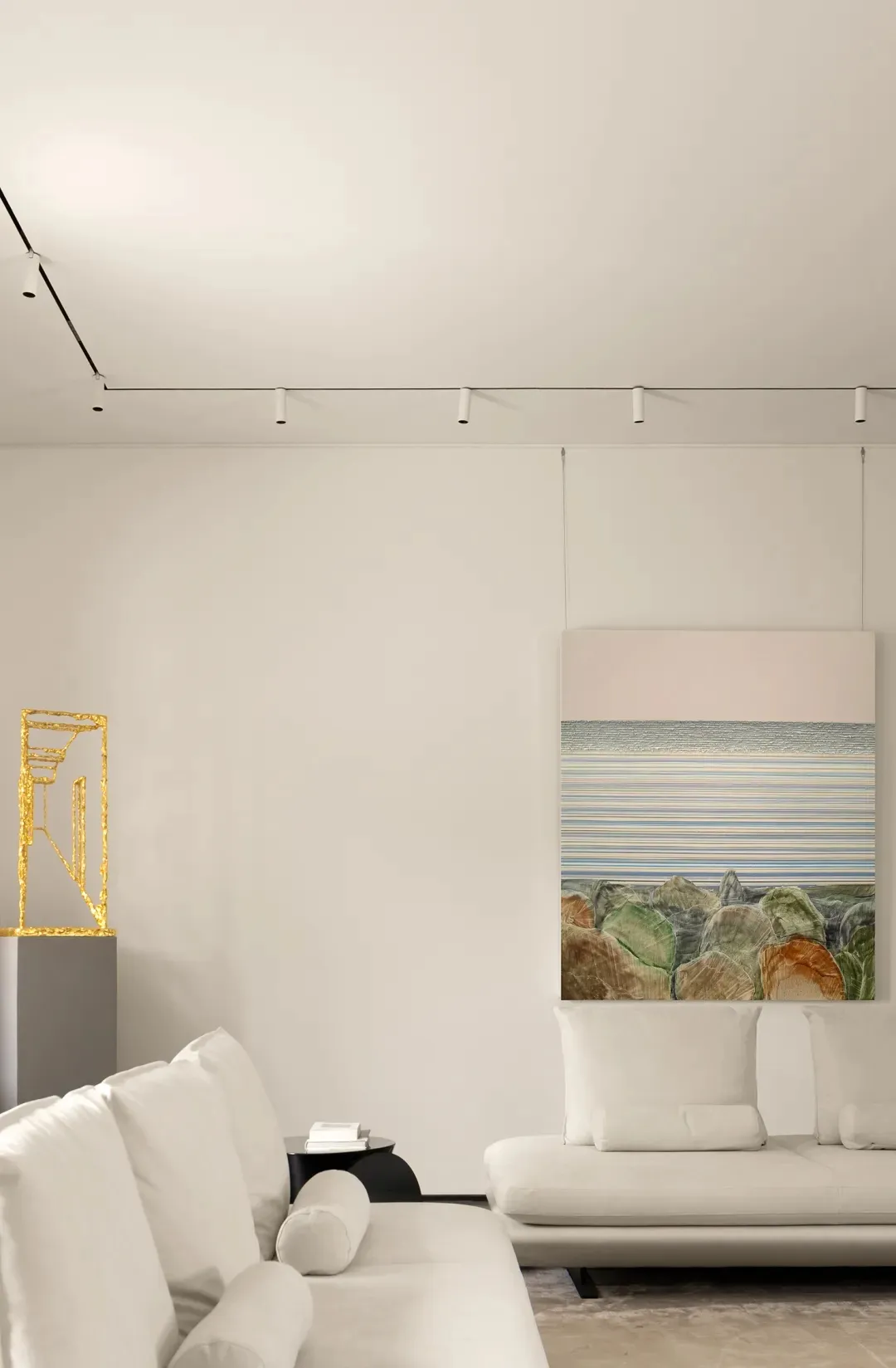 A modern minimalist living room with white sofas, textured fabric surfaces, and a geometric sculpture.