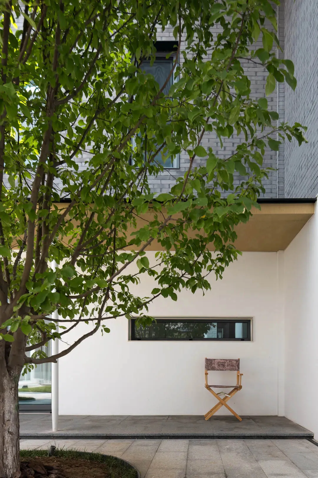 A minimalist modern building exterior made of concrete, featuring a tree and a director's chair.