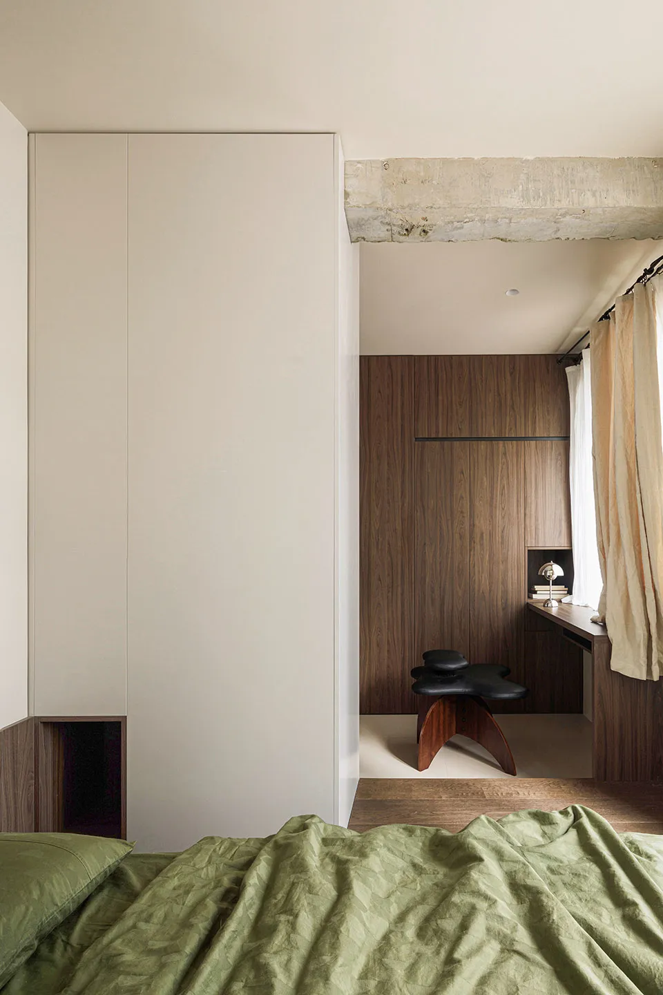 A minimalist bedroom featuring a wall cabinet with green bedding and a black stool.