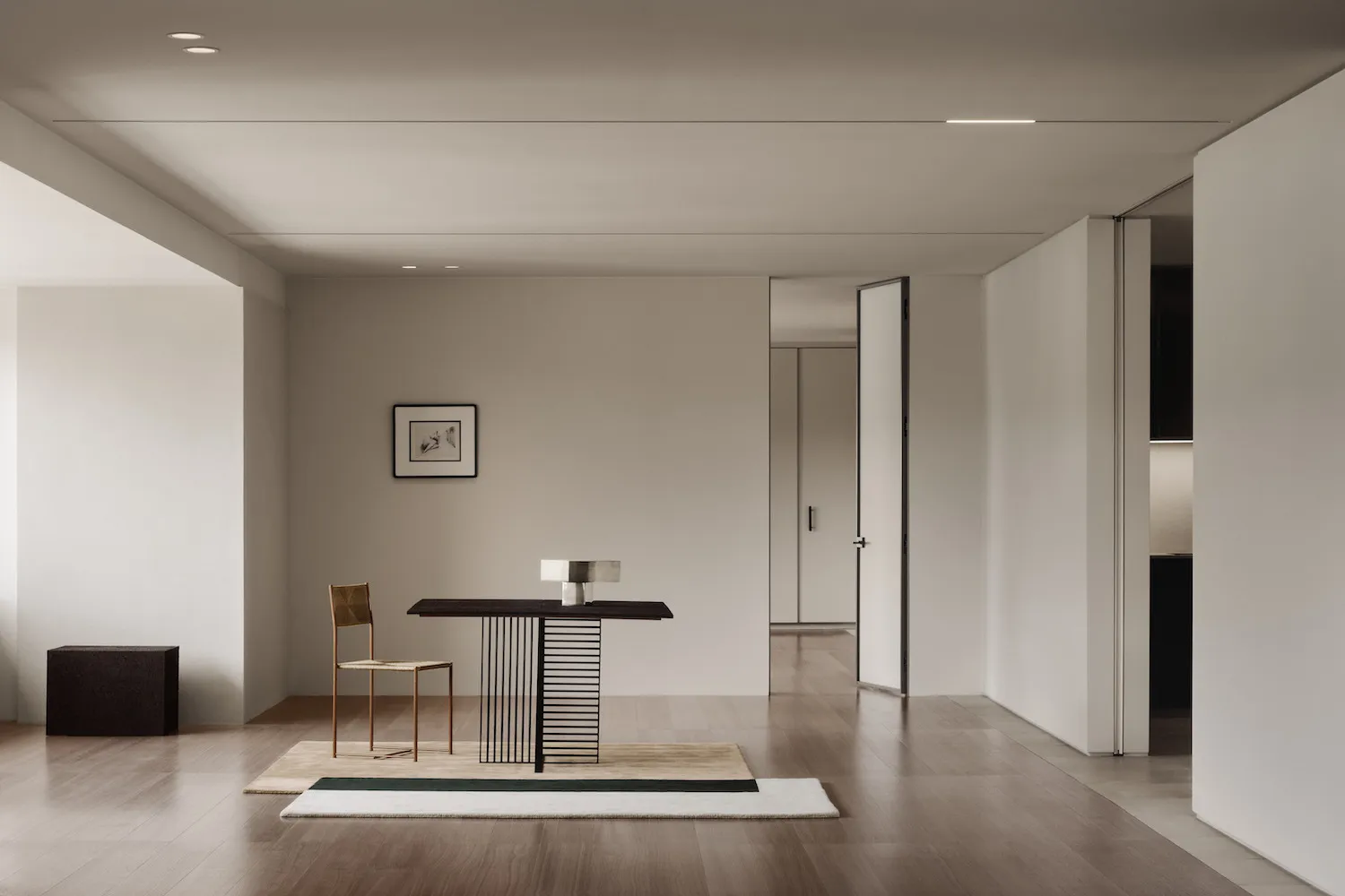 A minimalist interior featuring a metal console table with a black top, placed on a rug with green and beige tiles, next to a