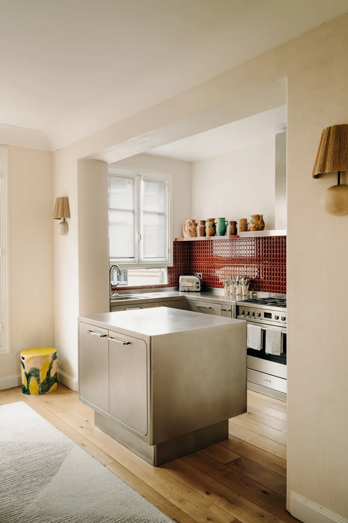 A minimalist kitchen with a metal island and a red-tiled backsplash.
