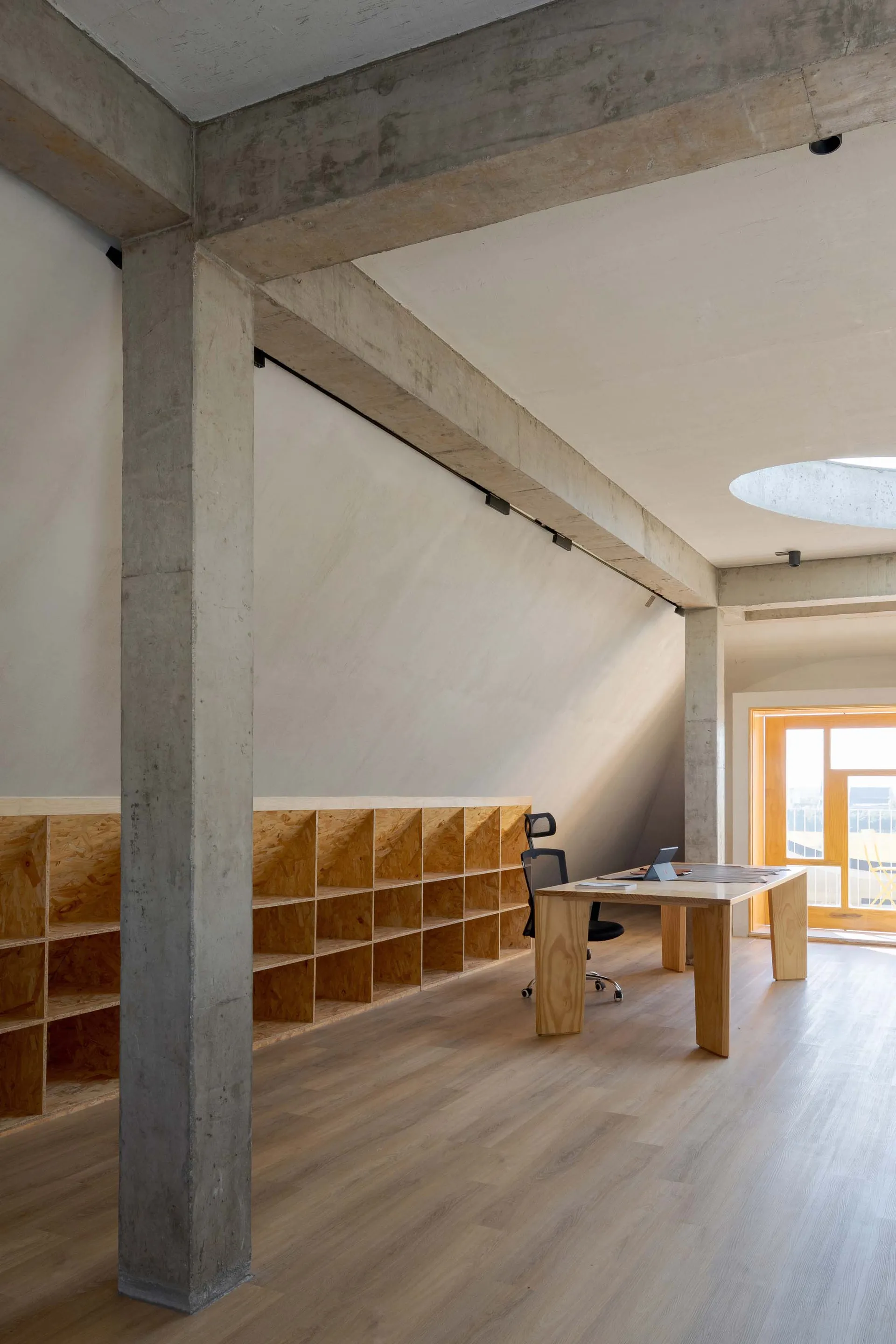 A minimalist office space featuring concrete walls and wooden furniture.