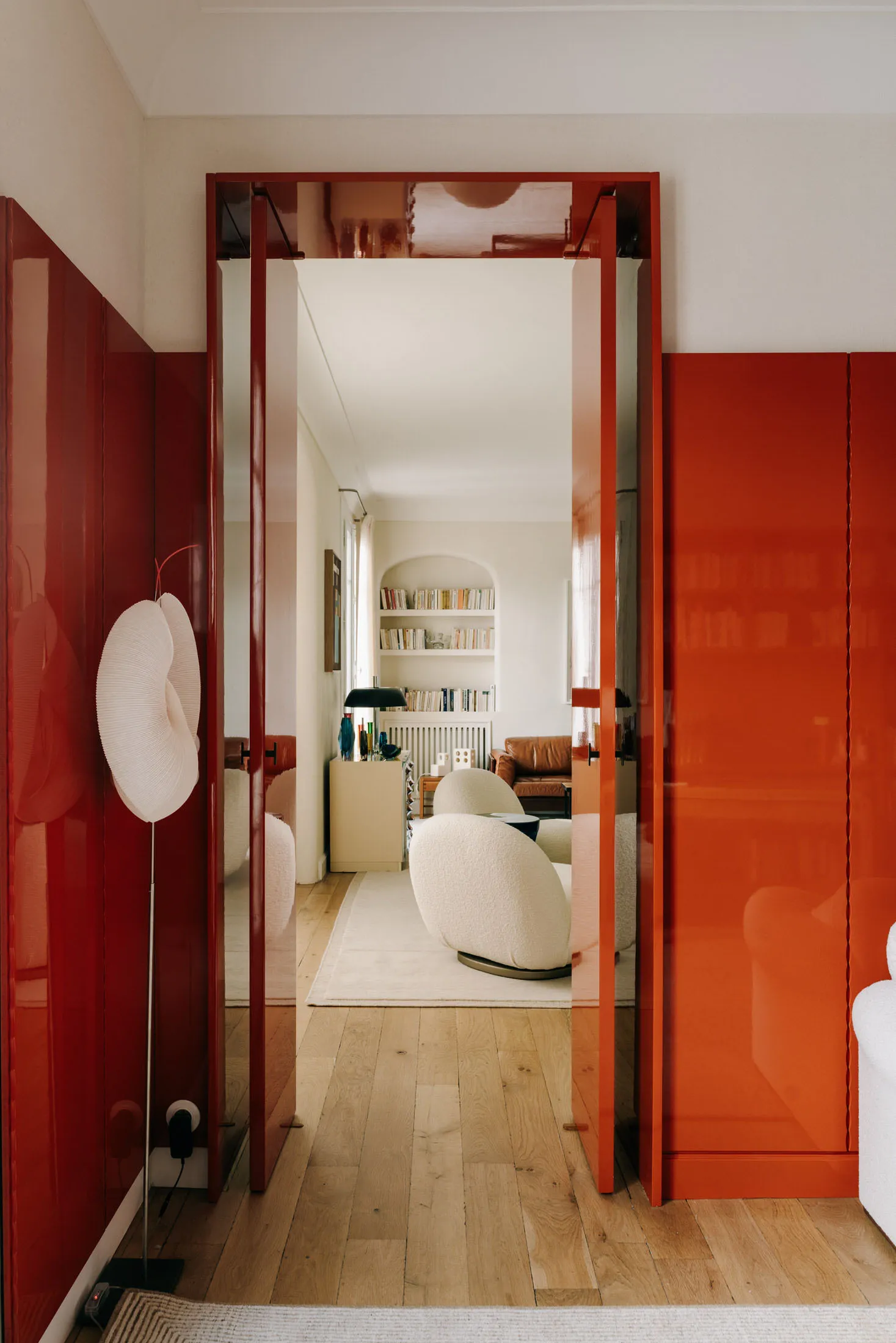 A minimalist interior with red acrylic walls and a view of a living room with modern furniture and bookshelves.