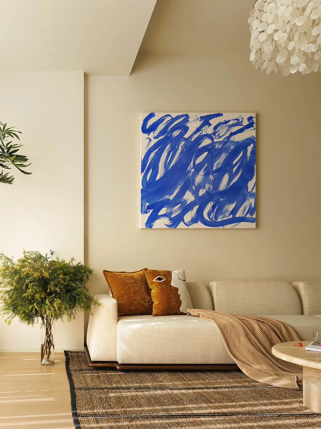 A minimalist living room featuring a white sofa with blue and white abstract art above, a wooden coffee table, and a woven ru