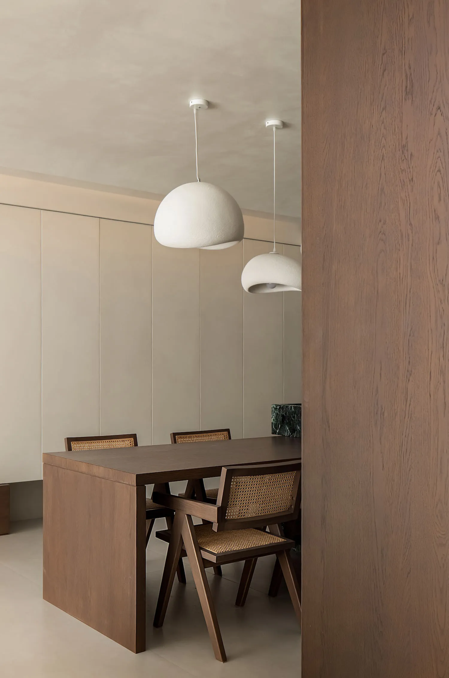 A modern dining room with wooden flooring, a wooden dining table, wooden chairs with wicker seats, and two white pendant ligh
